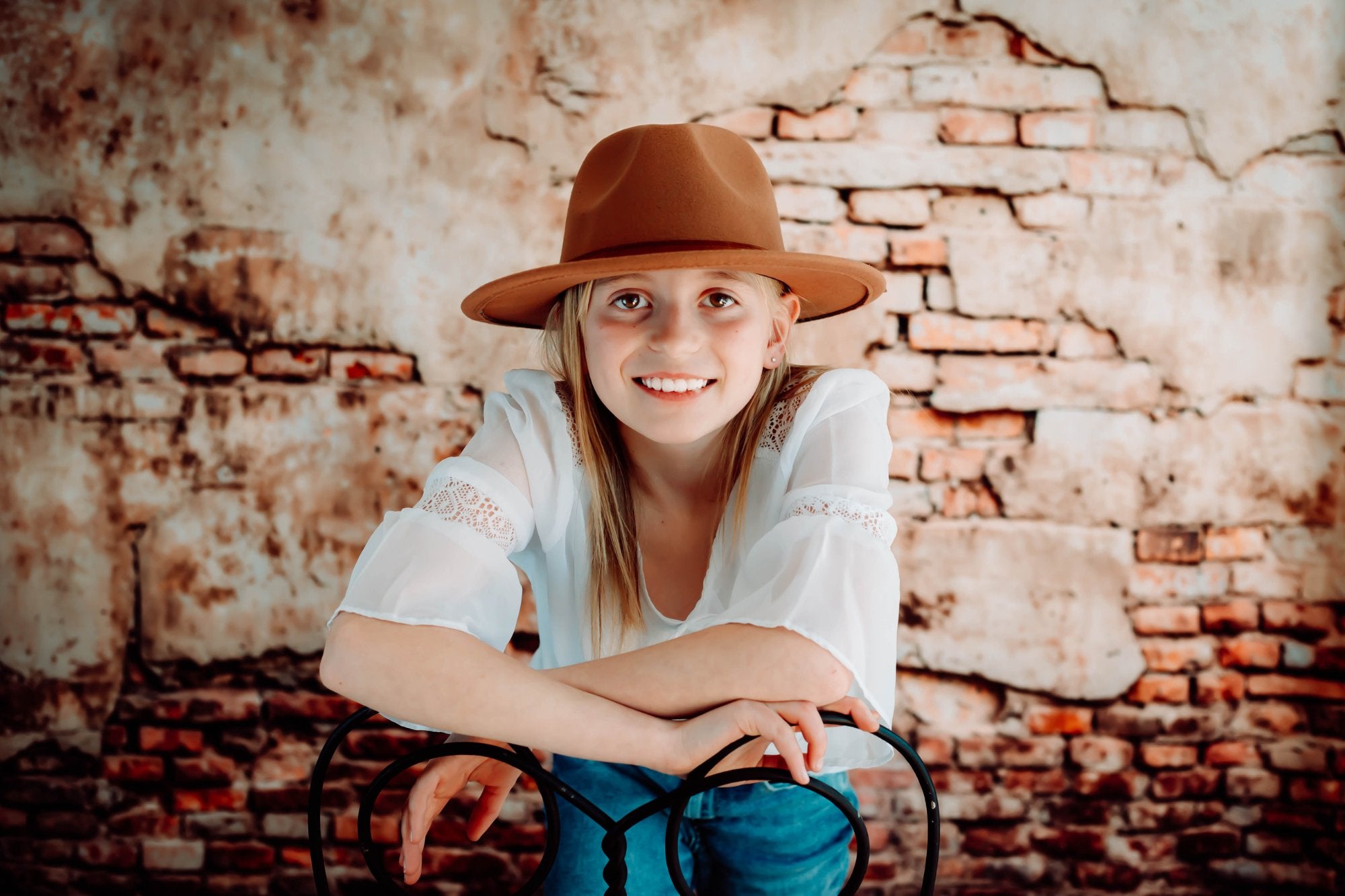 Une fille portant un chapeau se tient devant un fond de mur de briques beige-marron