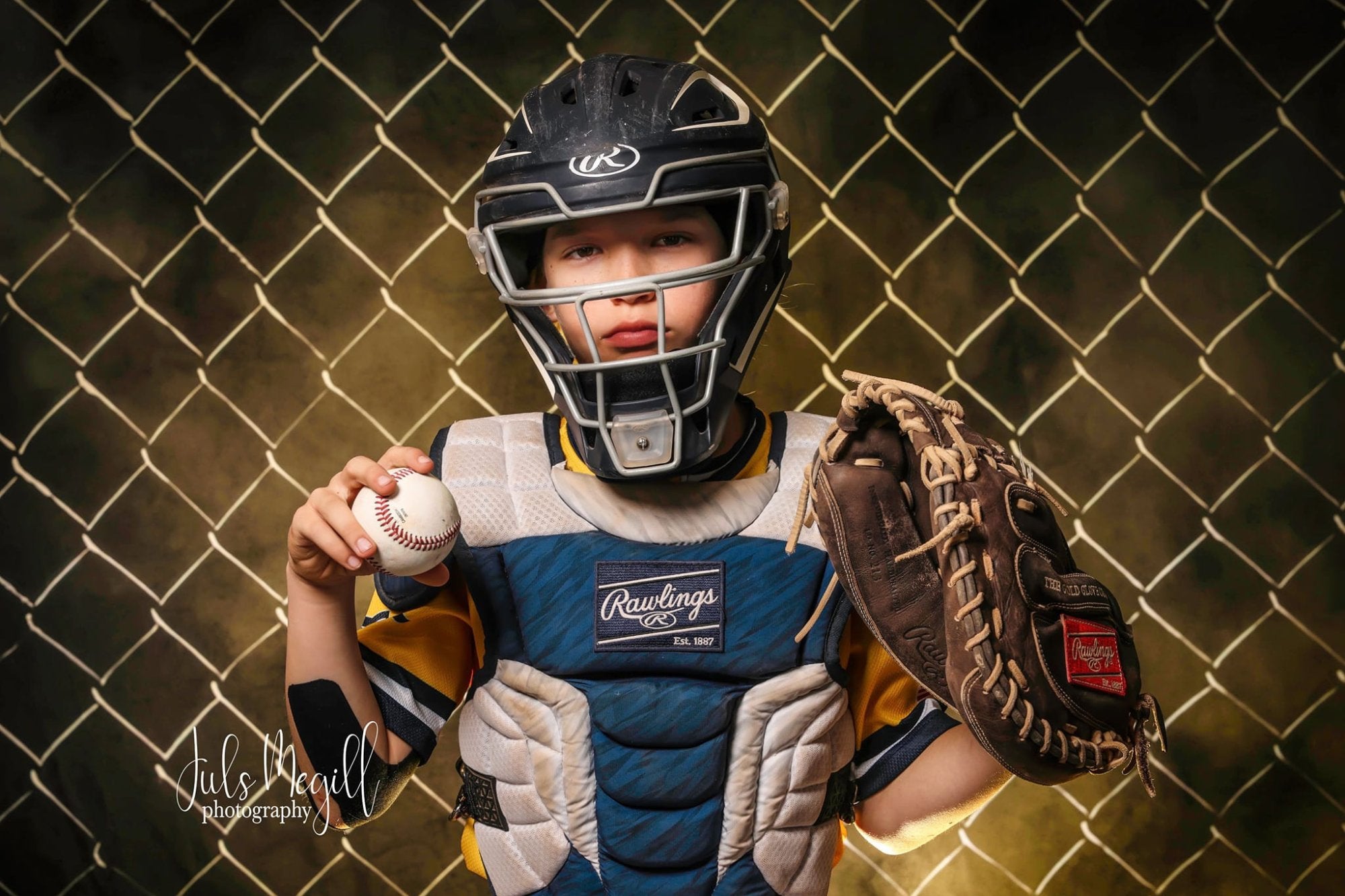 Un garçon en uniforme de baseball se tient devant un fond de barbelés avec une balle de baseball dans les mains