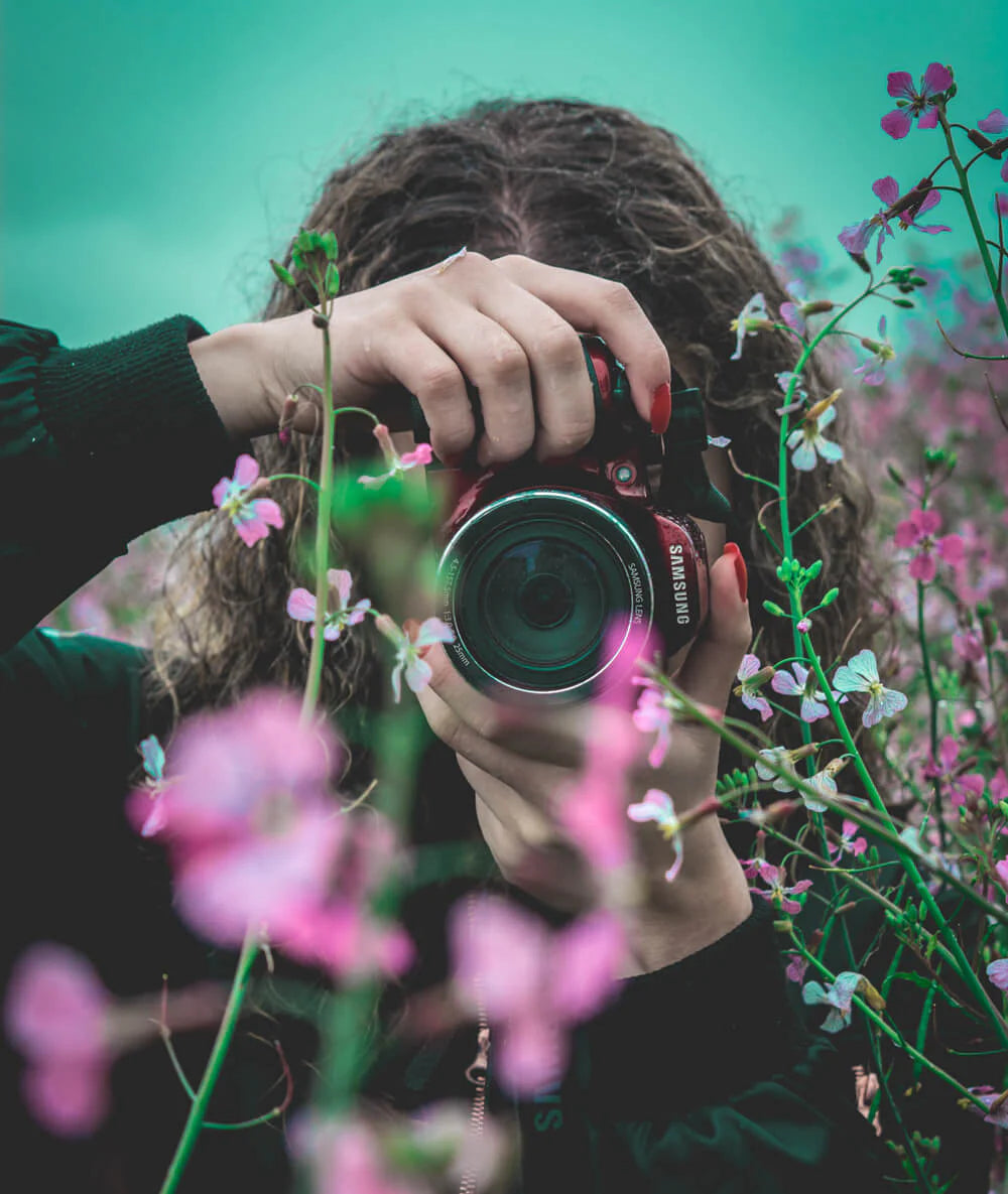 Une femme prend un appareil photo et prend des photos parmi les fleurs
