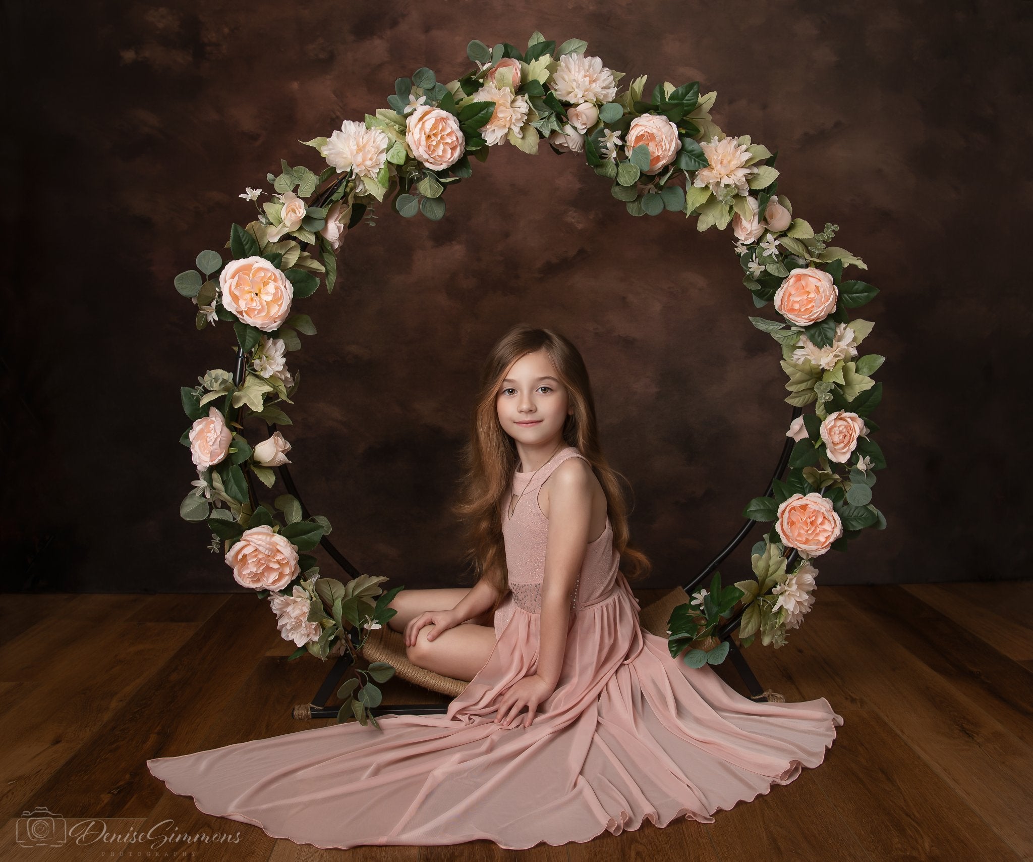 Petite fille assise sur un accessoire d'arche de fleurs devant un fond abstrait marron
