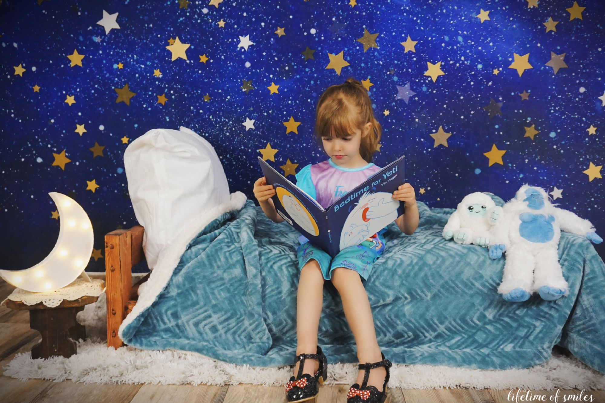 Une petite fille est assise sur le lit devant un fond de ciel étoilé et lit un livre de conte de fées