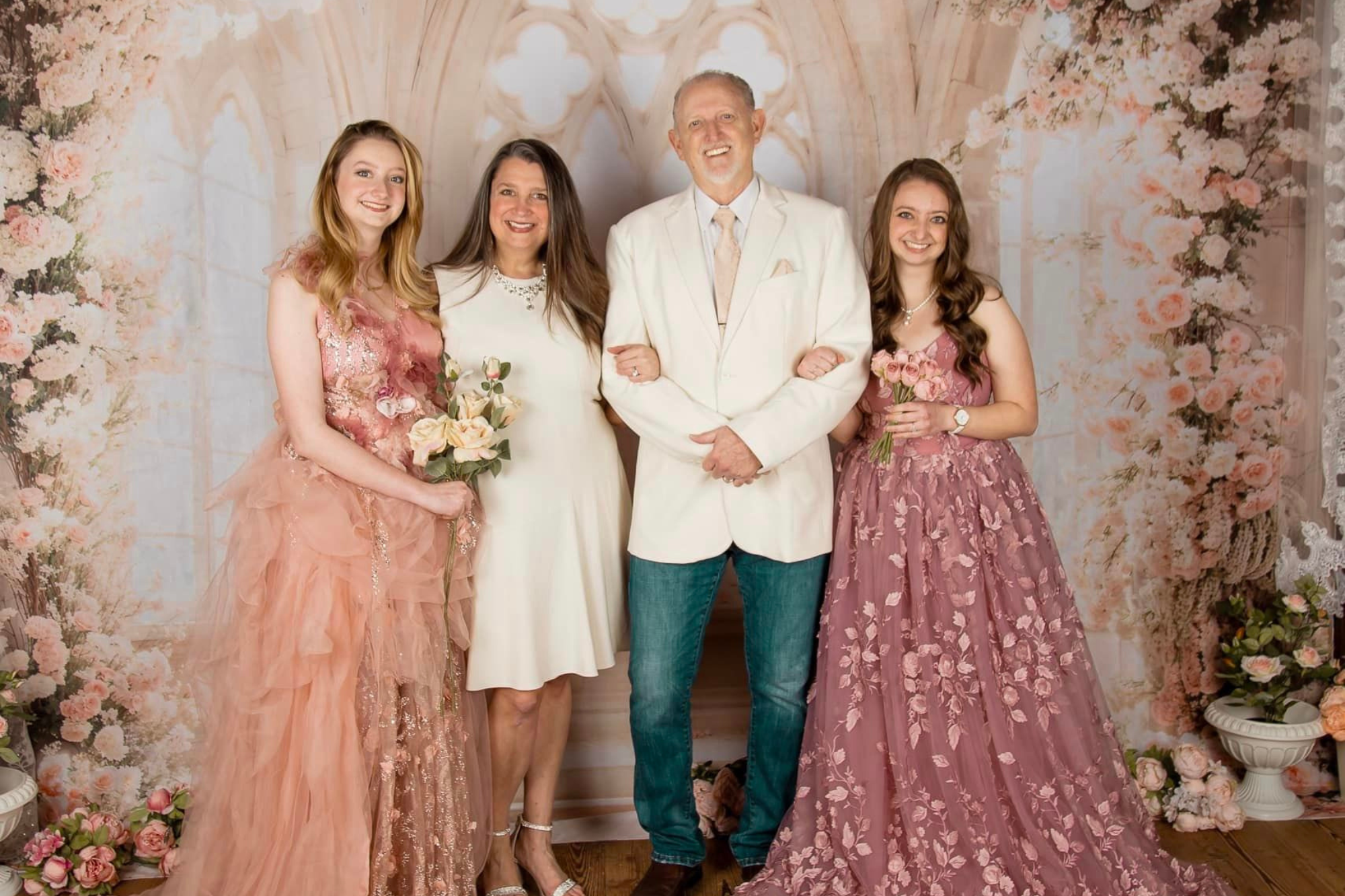 Maman, papa et deux filles debout devant un fond de fleurs sur le thème du mariage